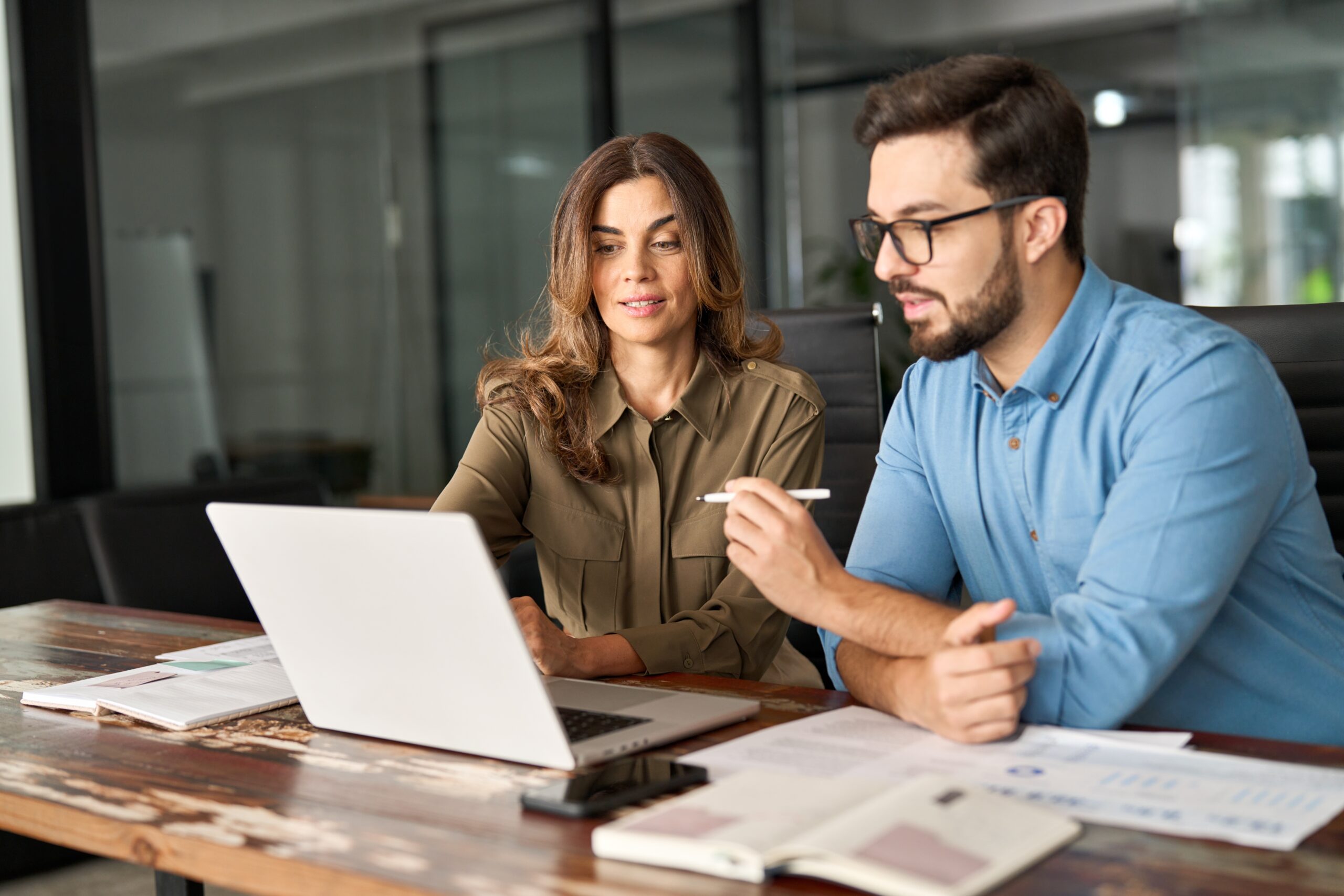 Two,Busy,Colleagues,Working,Together,Talking,Using,Laptop,In,Office. Nearshore support offers lower turnover